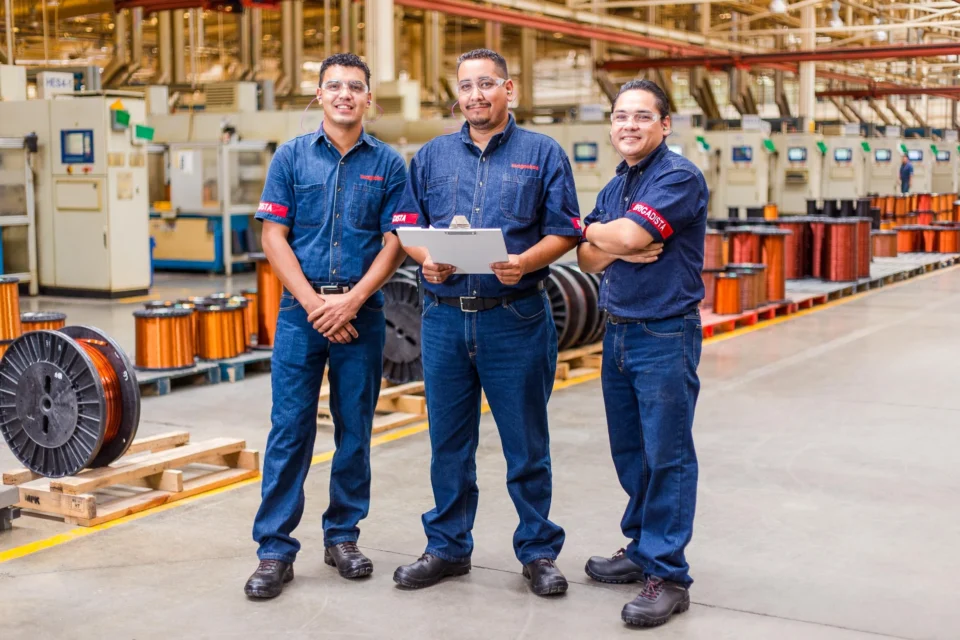 Equipo de trabajo en planta con maquinaria y materiales como contexto.