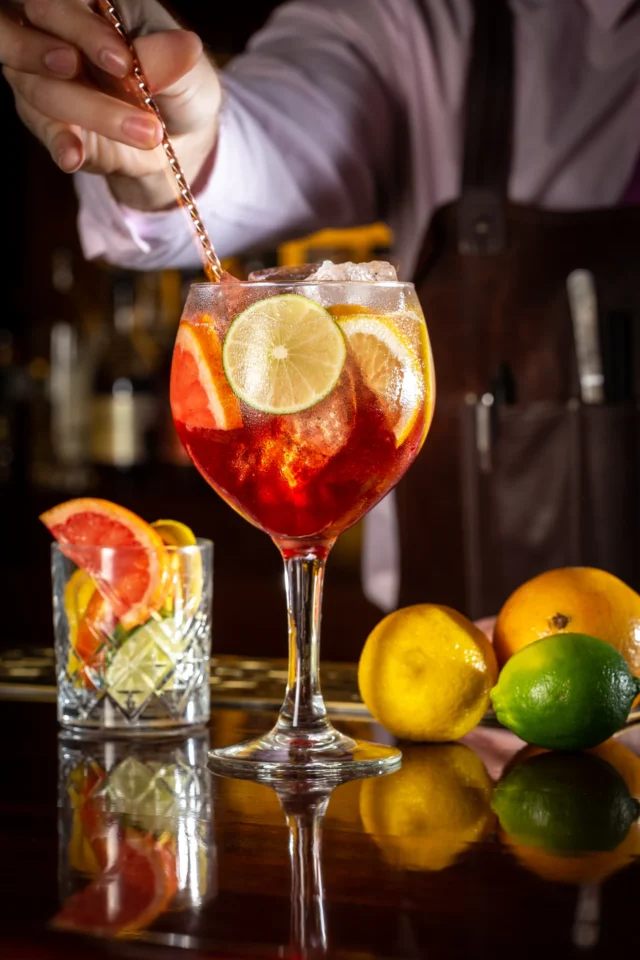 Coctelería con cítricos y el mixólogo preparando la bebida; color, transparencia y acción.